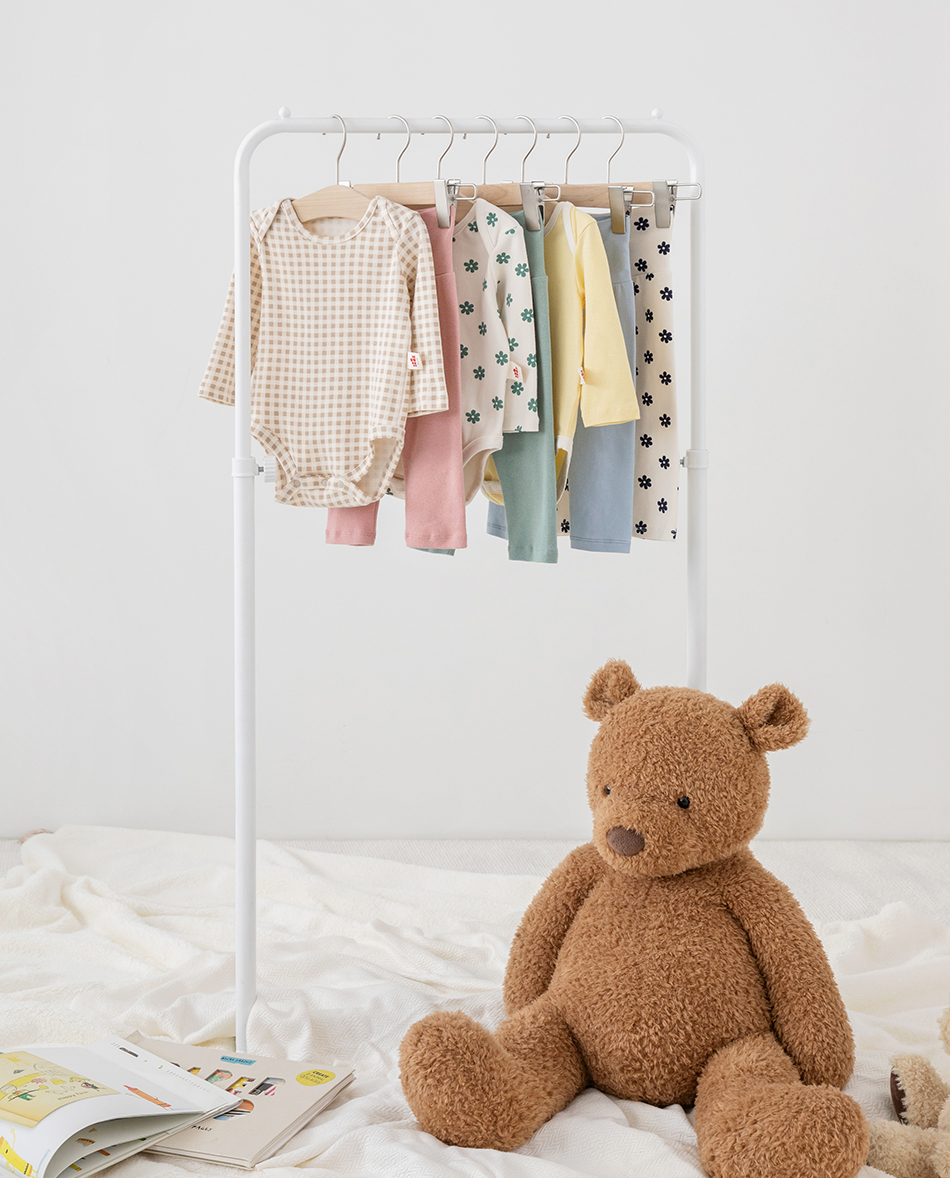 옷걸이에 걸려있는 여러벌의 아기옷과 갈색 곰인형